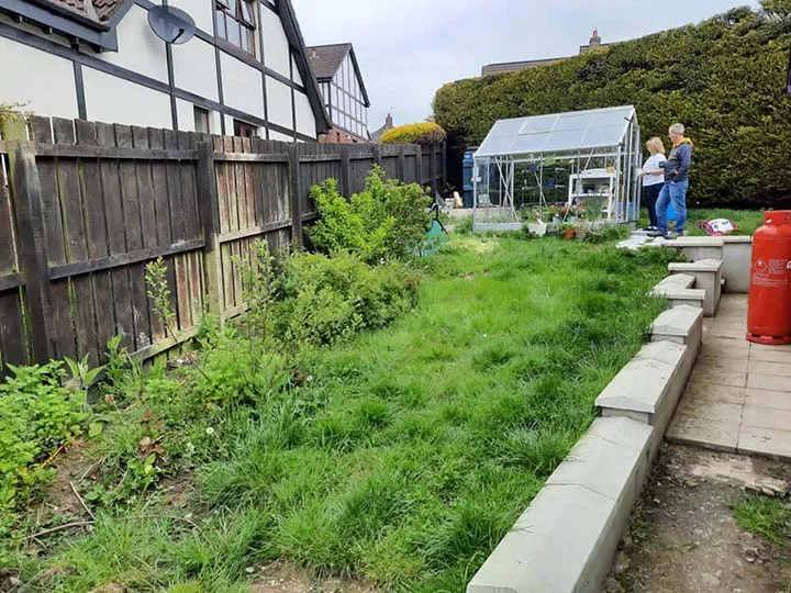 Overgrown garden and greenhouse beside the fence of a garden