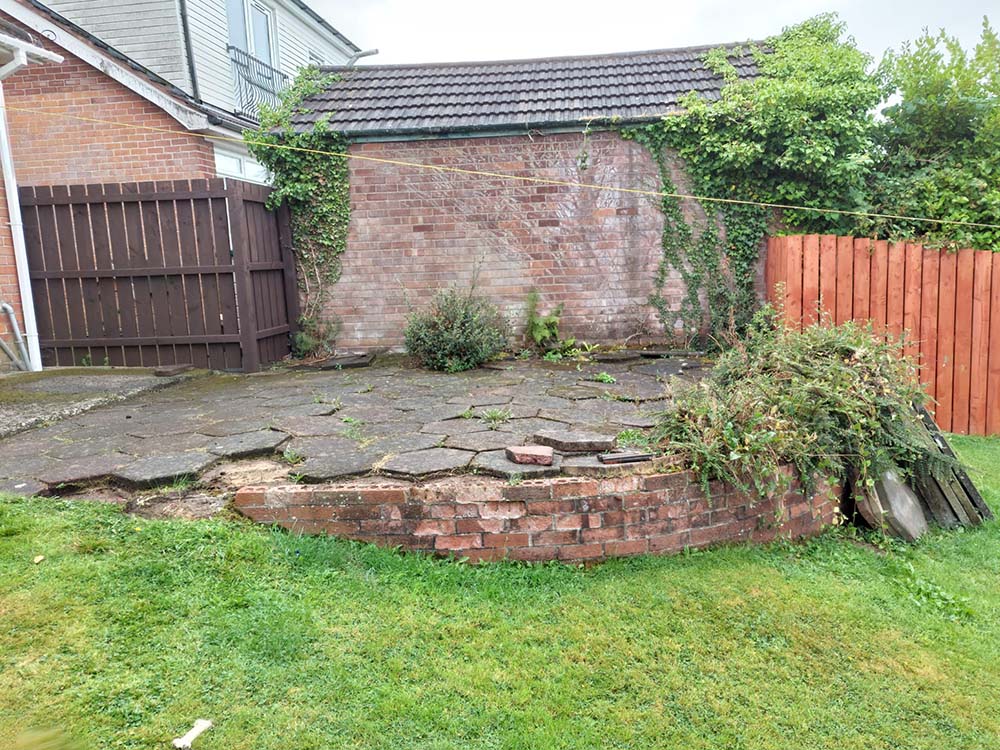 Old patio with broken paving slabs and an overgroth of weeds